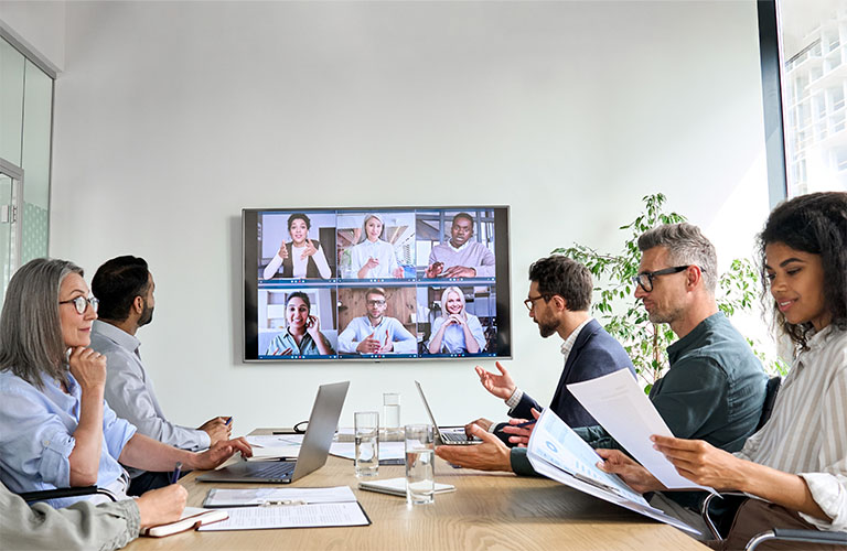 Office professionals participate in a hybrid (in-person and virtual) meeting.