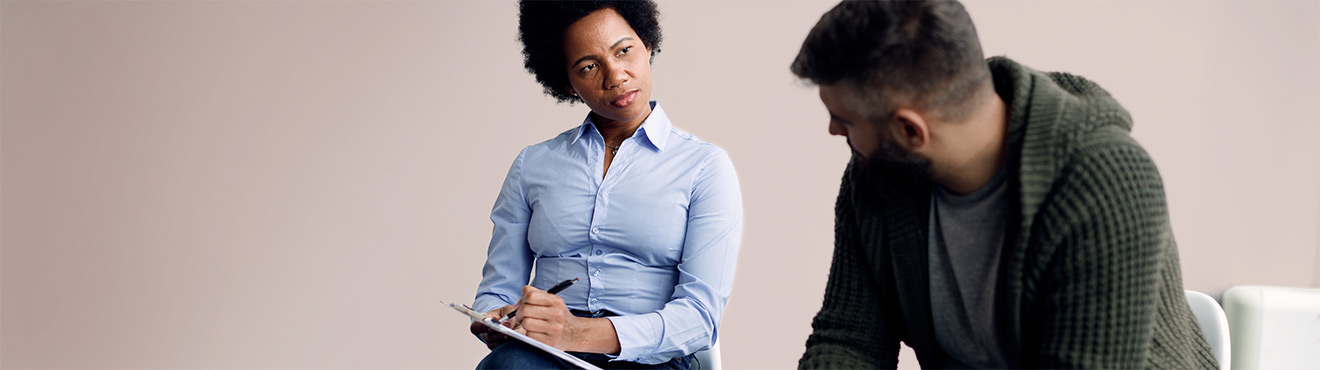 A person with a clipboard listening to a person who is leaning forward in a chair.