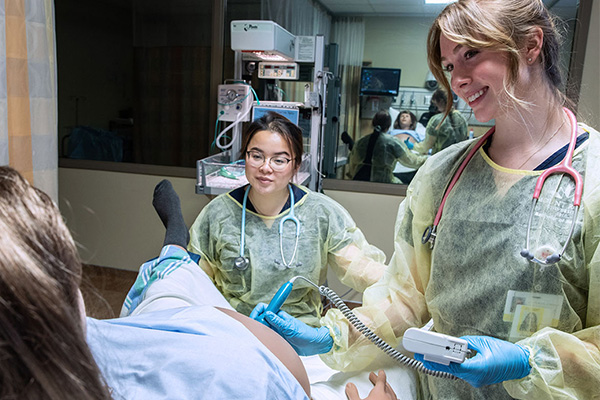 Two Mount Royal University midwifery students administering an ultrasound on a pregnant medical mannequin in the Health Simulation Learning Centre.