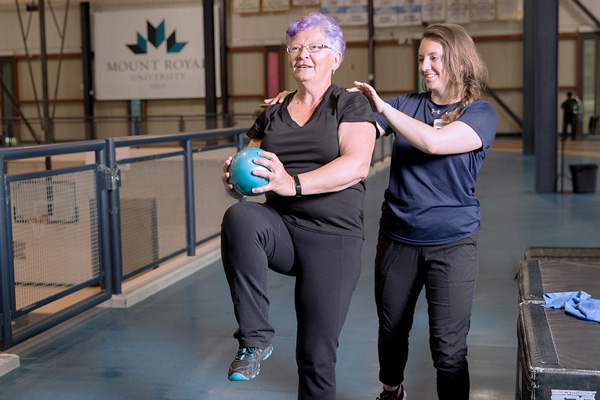 A senior patient holds a medicine ball while receiving guidance from a professional at the Mount Royal University recreation centre.