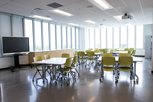 Image of a classroom. The space is set up with several chairs around communal desks.