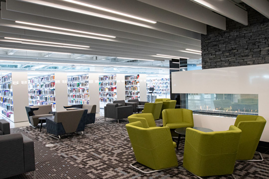 Photo of the fireplace lounge. Chairs are arranged near the fireplace with library collection int he background.