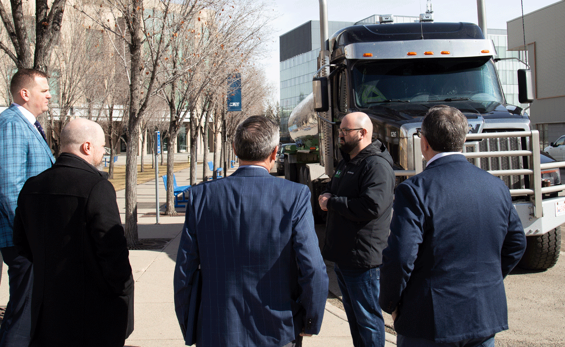 A group of men stand in front of a large truck, engaged in conversation.