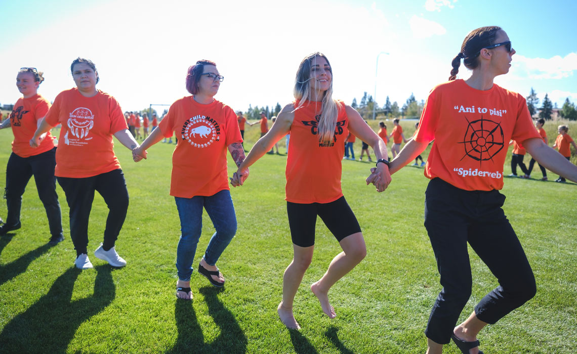 A group of people in orange shirts standing together, holding hands in a display of unity and support.