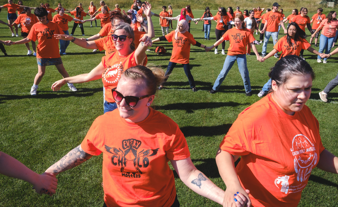 A group of people in orange shirts standing together, holding hands in a display of unity and support.