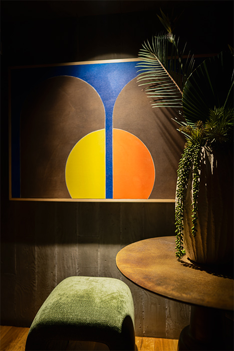A lamp illuminates a painting in a cozy bar setting, enhancing the warm atmosphere.