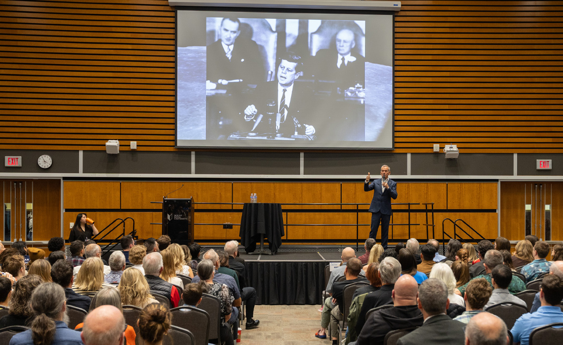 Colonel Chris Hadfield presenting to a large audience in a well-lit conference hall.