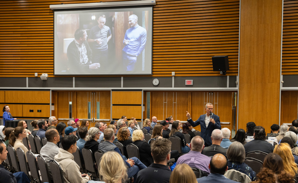 Colonel Chris Hadfield presenting to a large audience in a well-lit conference hall.