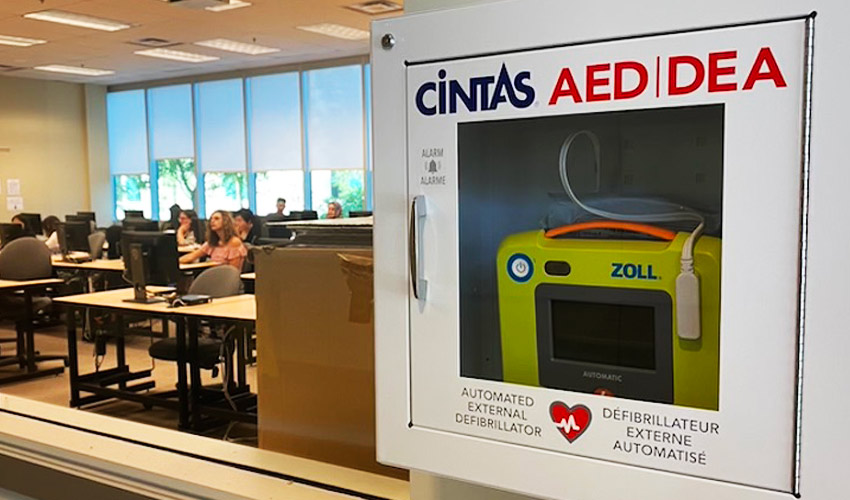 An automated external defibrillator mounted to the wall outside of a classroom in the Bissett School of Business.