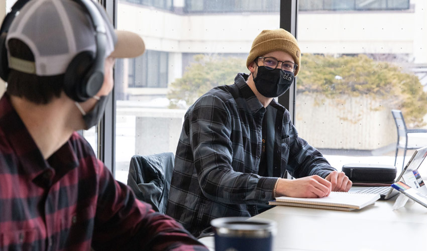 Two Mount Royal University students wearing masks and having a conversation on campus.