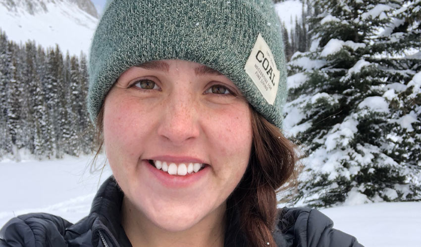 Briana Hamilton standing in front of evergreen trees covered in snow.