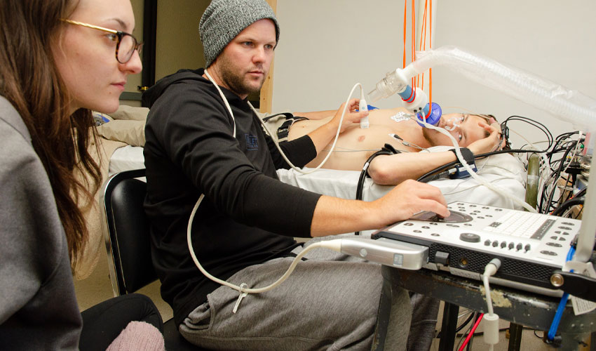 Photo of Britty Byman and Lindsay Boulet performing a echochardiography on Jordan Bird.