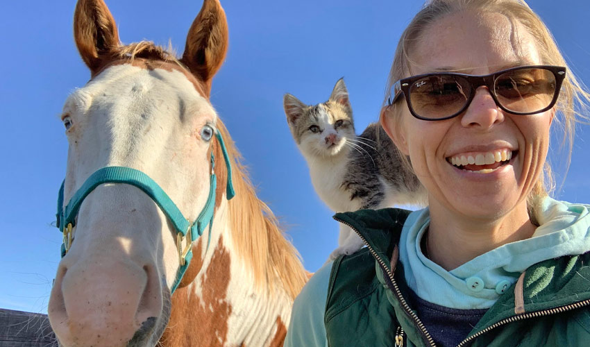 Dr. Carolyn Willekes poses for a photo standing next to a white horse.