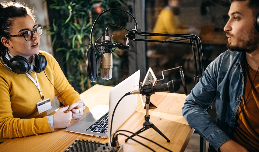 Two young people having a conversation in a radio station recording booth.