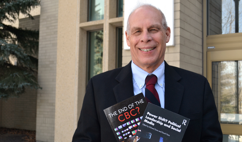 Dr. David Taras, PhD, holding two books. One he co-authored and the other co-edited.