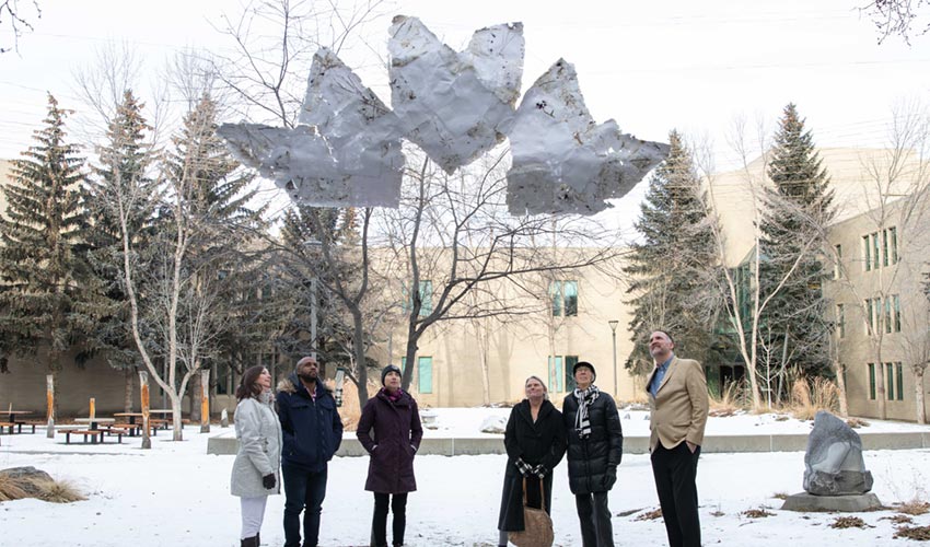 Students, the artist, donor and Stephen Price, dean of the Faculty of Community, Health and Education look up at the art hanging in the courtyard.