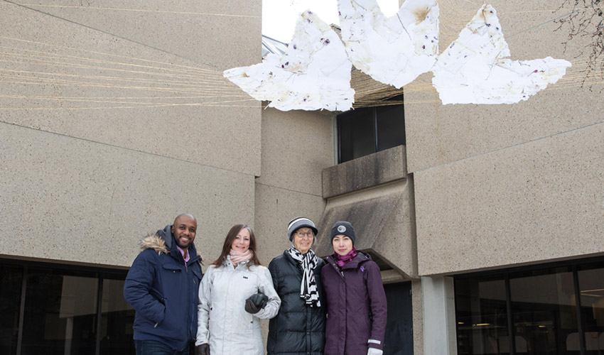 Students Dwayne Collins and Sheri H. Easterbrook pose with donor Agnes Cooke and artist Tamara Cardinal under the art piece hanging above.