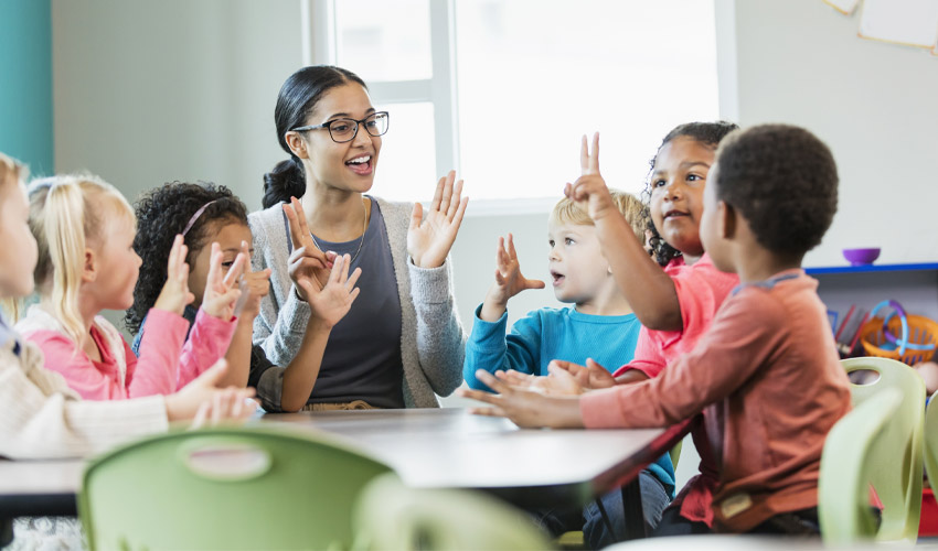 A teacher in the classroom with six young kids.