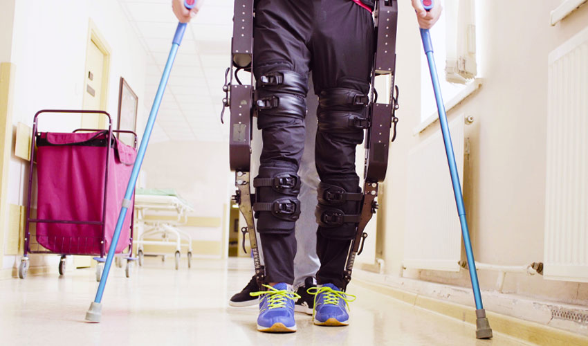 Legs of man in the robotic exoskeleton walking through the corridor of the rehabilitation clinic.