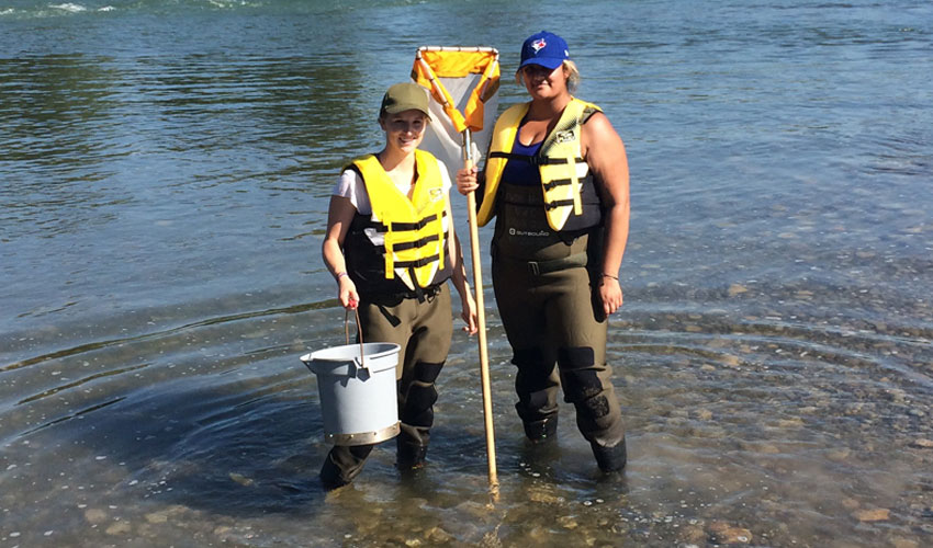 Photo of Danielle Dusome and Hannah Grewal collecting water samples in the Bow River.