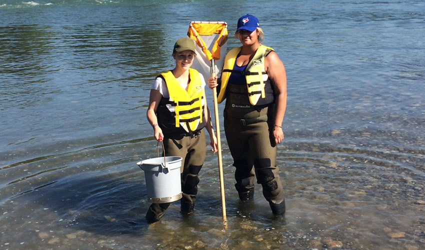 Photo of Danielle Dusome and Hannah Grewal collecting water samples in the Bow River.