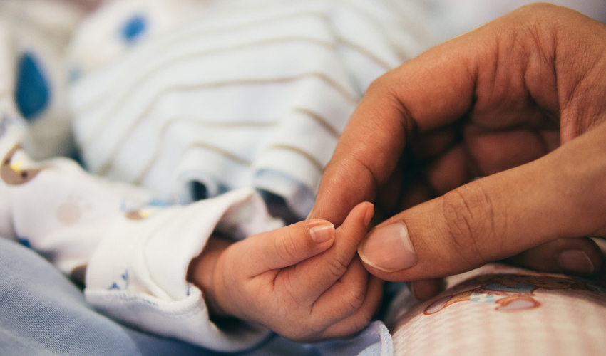Photo of baby’s hand being held.