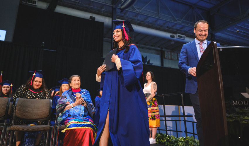 Katea Kootenay from Bearspaw First Nation, Treaty 7, crosses the stage after receiving her Indigenous University Bridging Program (IUBP) certificate from administrator Tori McMillan, member of the Berens River First Nation, Treaty 5, right. Cree Elder Doreen Spence, seated, also attended the Indigenous Graduation Celebration held at Mount Royal on June 6. Kootenay has applied to the Bachelor of Arts Psychology and the Bachelor of Arts — Sociology for the Fall 2022 semester.