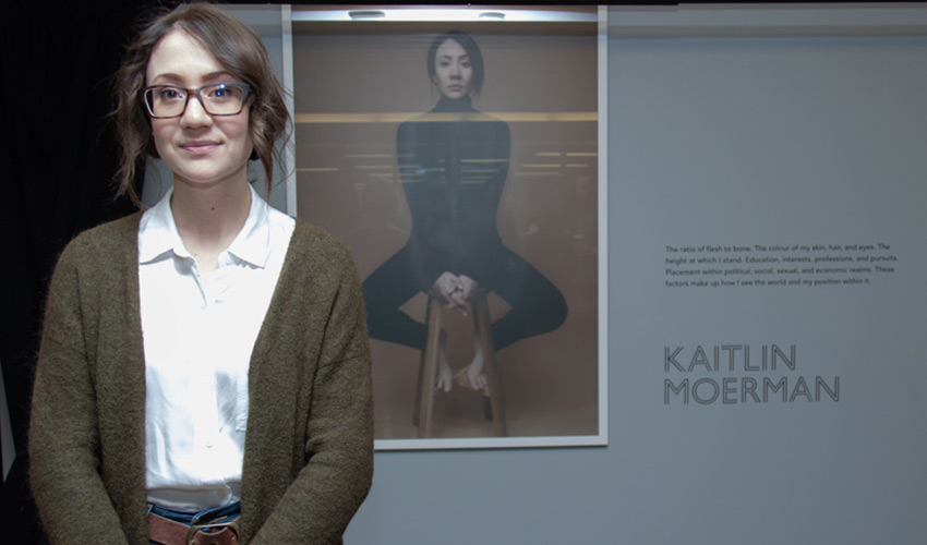 Kaitlin Moerman stands in front of a photography self-portrait
