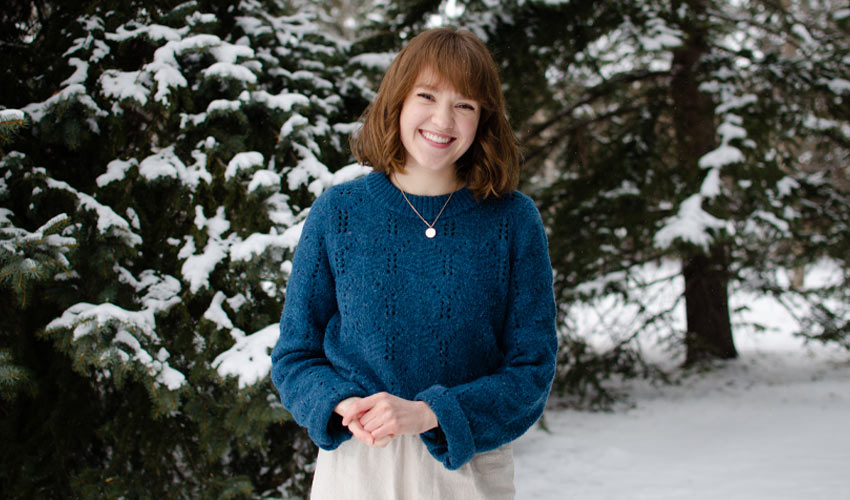 Laura Alwast standing in front of evergreen trees covered in snow.