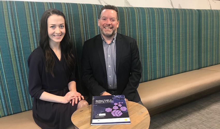 Anna Johnson and James Stauch pose with a physical copy of The Student Guide to Mapping a System