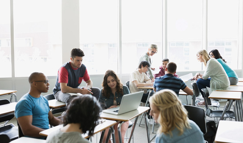 Young woman using laptop with students watching and smiling.