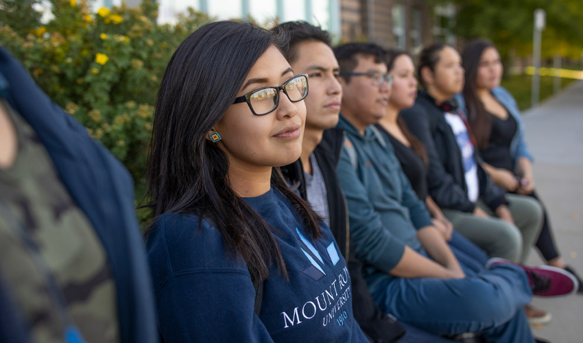 A group of Mount Royal University students sitting in front of the MRU west residence.