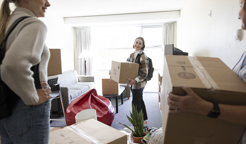 Student who is moving into MRU Residence stands in apartment unit holding a box.