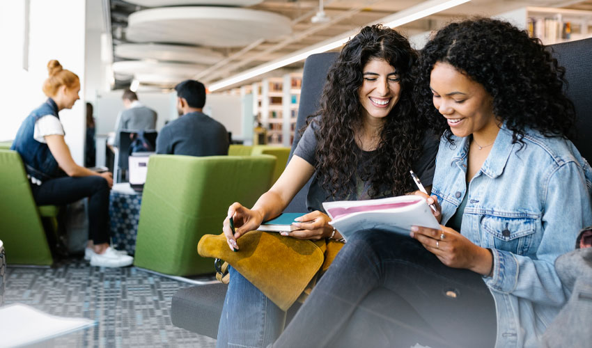 A group of students in the MRU Library smiling and collaborating on a task.