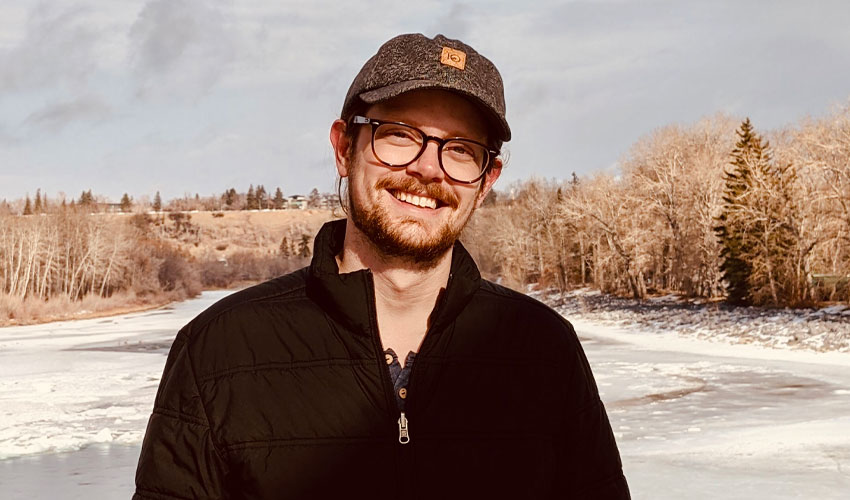 Tim Hilton stands on a bridge in Calgary with the bow river in the background.