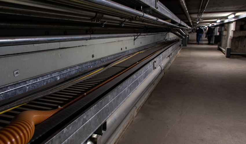 At left are the cable trays, which once supported large bundles of bulky, heavy cables that have now been replaced with much smaller ones still carried by the tray. The tray runs the full length of the tunnel, connecting important lines to the University’s data centre. The Main Street elevator shaft is embedded in concrete, seen on the right.