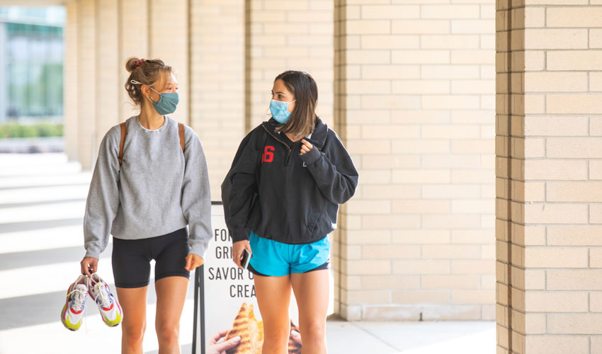 Two Mount Royal University students walking outside next to the Faculty of Arts building.