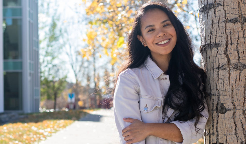 Whittnie Gaqui smiling while standing next to a tree on a beautiful fall day.