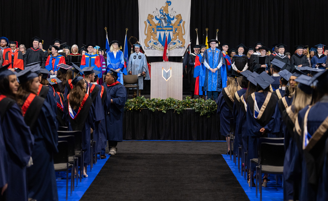Graduates in caps and gowns poses together in front of a stage, celebrating their academic achievements.