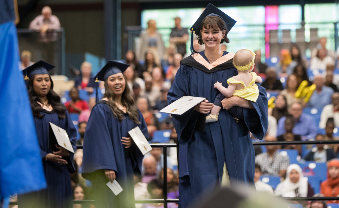 An MRU graduate smiling while crossing the stage; holding her baby.