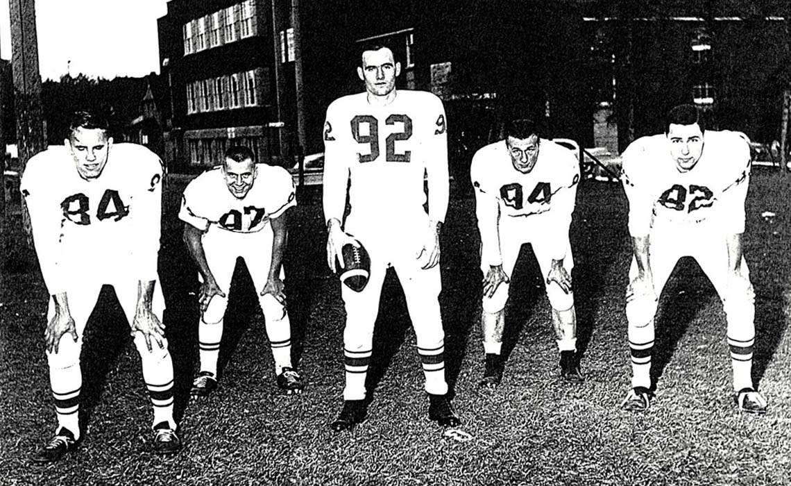 Old photo (from left to right) of Gerry Shaw, Ro Riley, Larry Robinson, Bill Goods and Dennis Stiles in their football uniforms standing in a line.