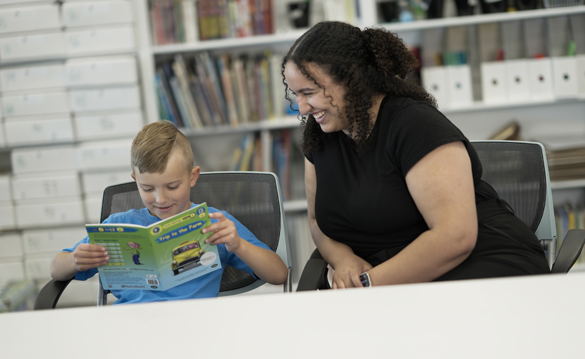 A woman and a boy reading a book while sitting at a table.