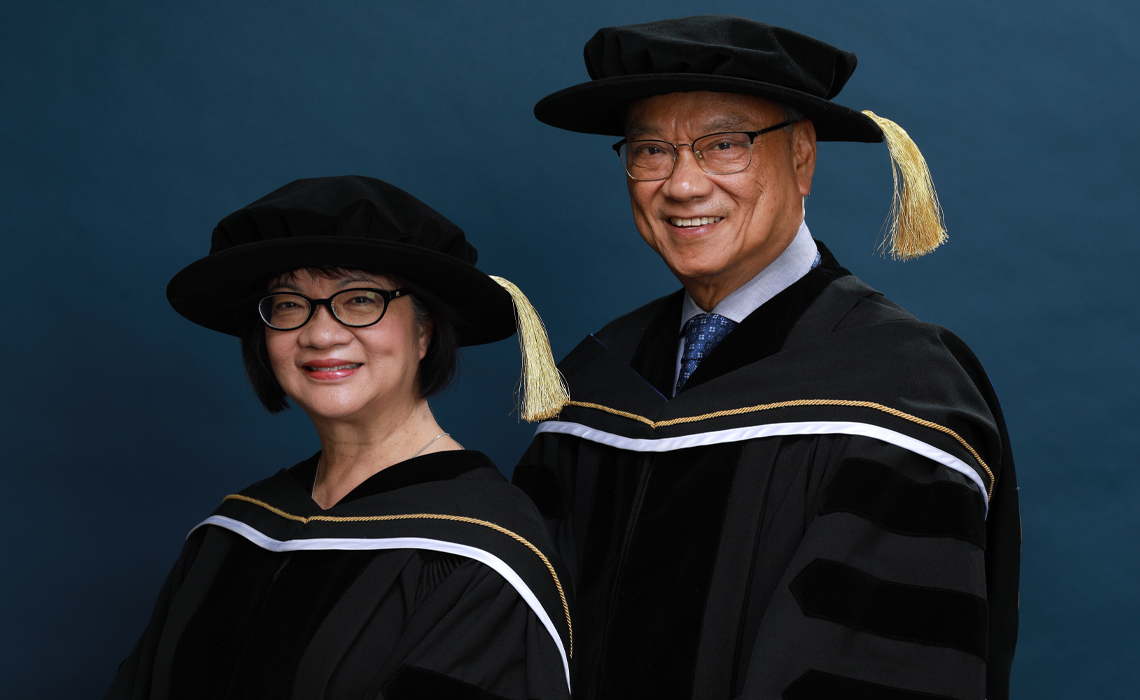 Eleanor and Wayne Chiu in graduation robes and caps pose together.