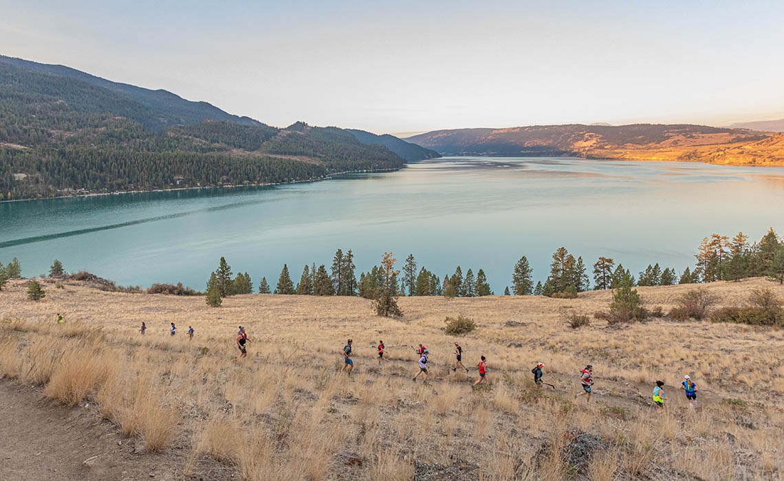 A group of runners on a winding trail near a serene lake.