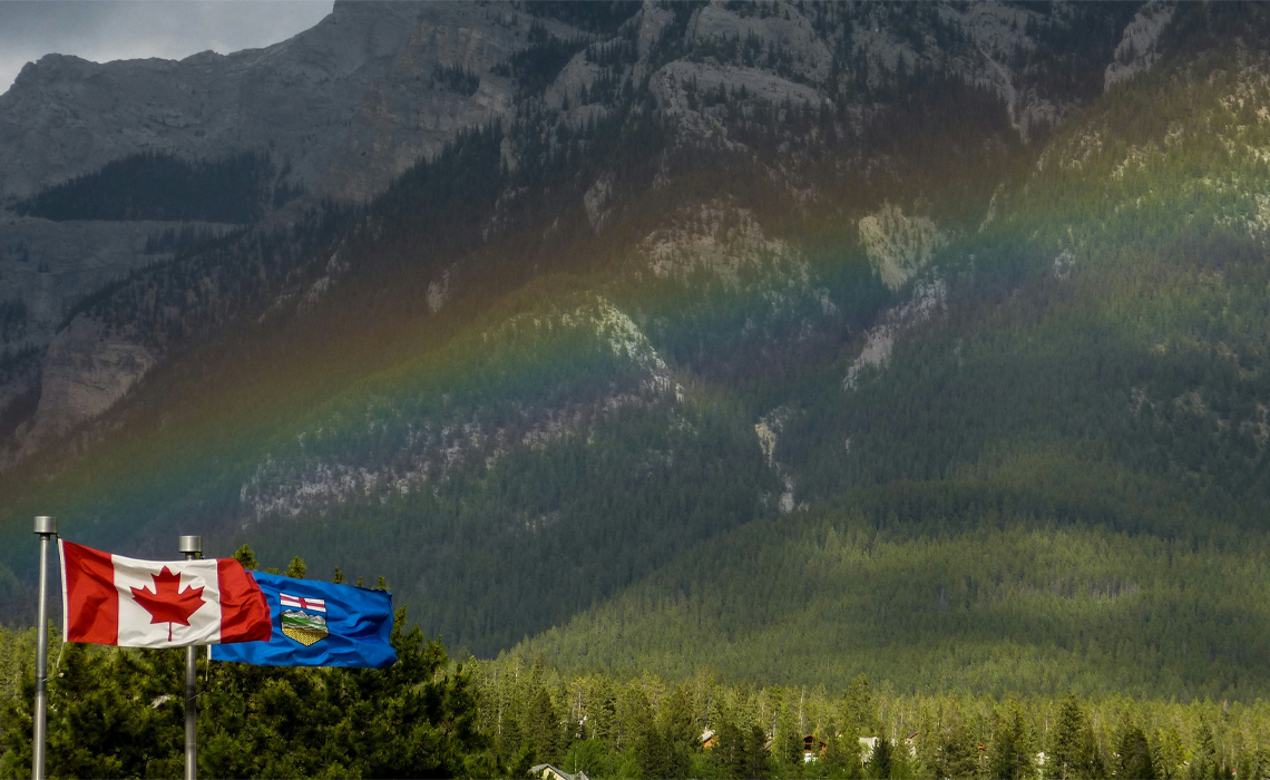 Two flags, Canada and Alberta, wave in the foreground, set against a majestic mountain backdrop.