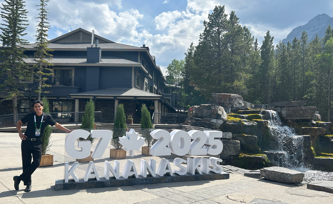 Gerardo Soriano stands stands in front of a sign displaying G7.