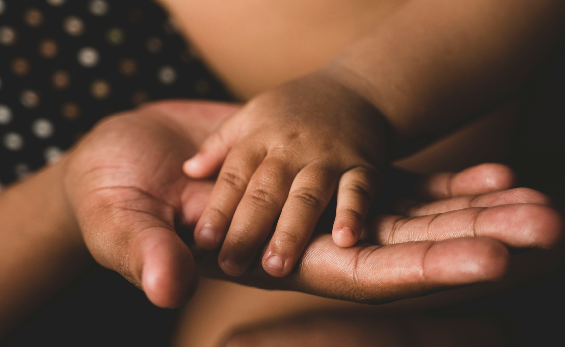 A child's small hands gently clasping a parent's hand, symbolizing love and connection.