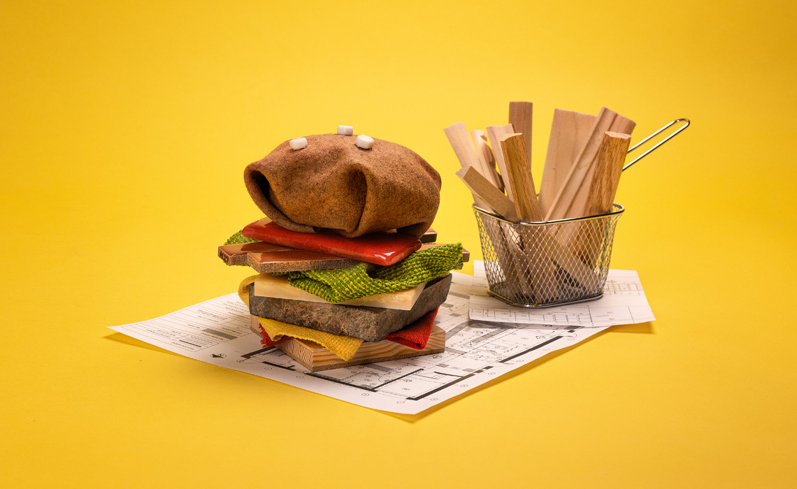 A hamburger and a cup of fries made from a blend of fabric and wood placed on a table.