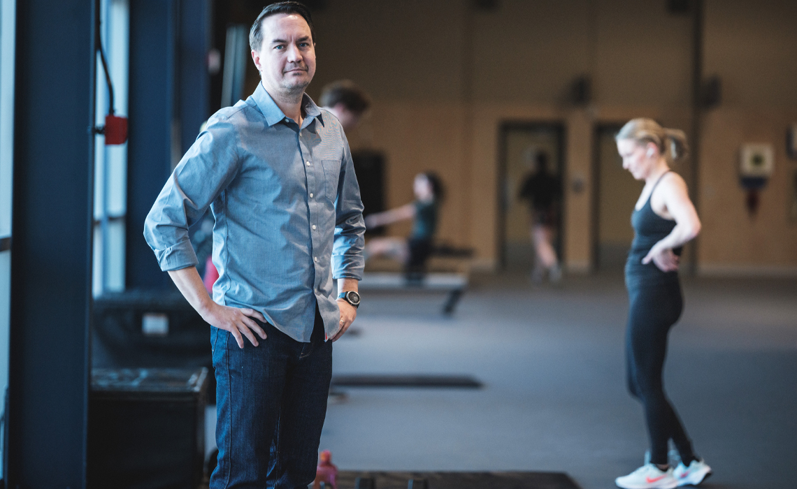 Jared Fletcher stands in the gym with several people exercising in the background.