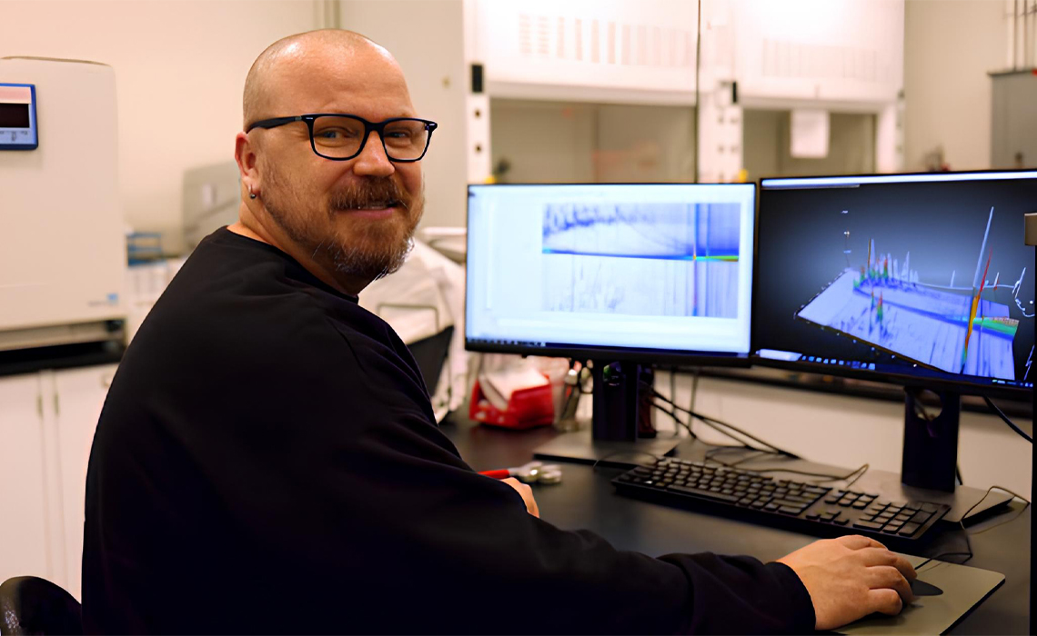Hayes is seated at a desk, utilizing two computer screens for his work activities.